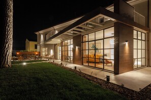 A modern house with large glass windows, a patio with outdoor furniture, and a well-lit interior. - Villa Francesca Relais (Gradara)