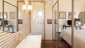 A modern hotel room with a large mirror, a white bathtub, a vanity with a gold faucet, a bed, and a desk with a laptop. - Villa Francesca Relais (Gradara)