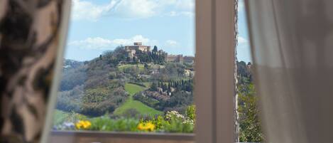 A balcony with a view of a castle on a hill, surrounded by greenery.