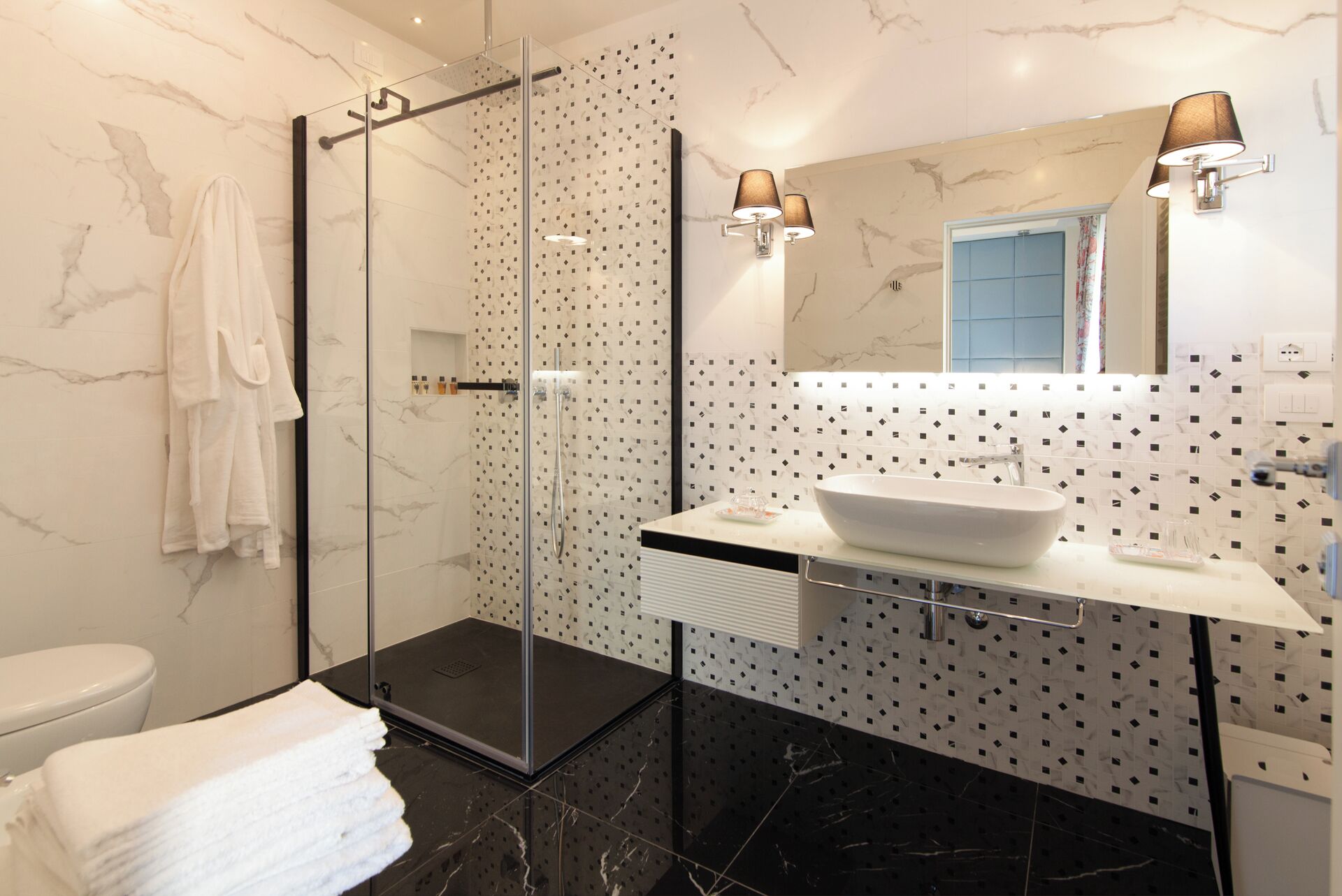 Un baño moderno con cabina de ducha de vidrio, un lavabo blanco con pileta integrada y pared de mármol con patrón geométrico.