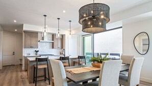 A modern kitchen with a central island, pendant lighting, and a dining area with a table and chairs. - Desert Dream Villa at Desert Color By Ember Stays (St. George)