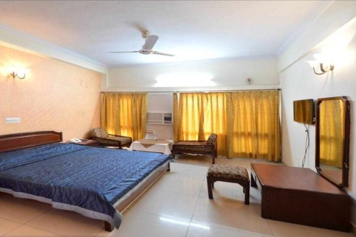 A hotel room with a bed, bedside table, chair, desk, and a ceiling fan.