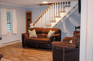 Una sala de estar con un sofá de cuero marrón, una escalera de madera y una estantería.