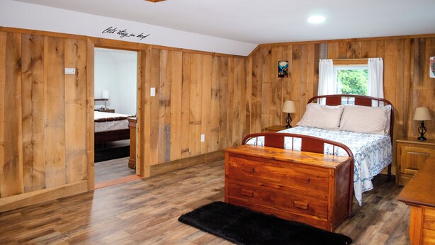 A wooden-paneled bedroom with a bed, bedside tables, and a black rug. - DLT Cabins, LLC - Holler Hideaway Cozy house sleeps 4 on 10 Minutes from SNP (Luray)