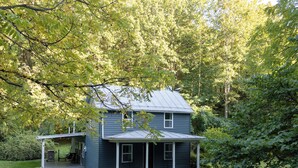A two-story house with a porch, surrounded by a wooded area. - DLT Cabins, LLC - Holler Hideaway Cozy house sleeps 4 on 10 Minutes from SNP (Luray)