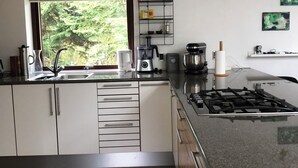 Una cocina moderna con estufa a gas, armarios empotrados, un ventanal con persianas y vistas a zonas verdes.