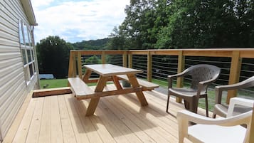 Un terrazzo in legno con tavolo da picnic e sedie di plastica, con vista su un paesaggio verde.