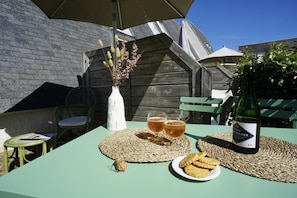 Un espace de restauration en plein air avec une table dressée pour deux personnes, agrémentée d’une bouteille de vin, de verres et d’une assiette de nourriture.