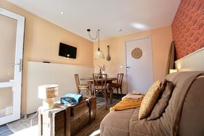 Uma sala de estar acolhedora com um sofá, uma mesa com cadeiras, uma televisão na parede e uma porta com um enfeite decorativo.