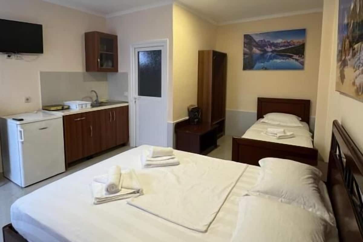 Una habitación de hotel con una cama grande, una kitchenette pequeña, un televisor y un cuadro en la pared.