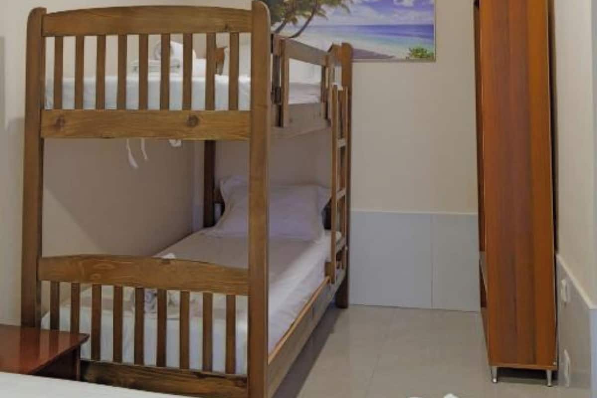 Dormitorio con literas, cabecera de madera, un cuadro de una escena de playa y un armario alto de madera.