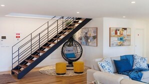 A modern living room with a staircase, a hanging chair, and a sofa with patterned cushions. - Vista D'Ouro- Luxury Villa in the mountains (Lavradas, Ponte da Barca)