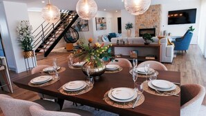 A dining area with a wooden table set for six, surrounded by chairs, with a staircase and living area in the background. - Vista D'Ouro- Luxury Villa in the mountains (Lavradas, Ponte da Barca)