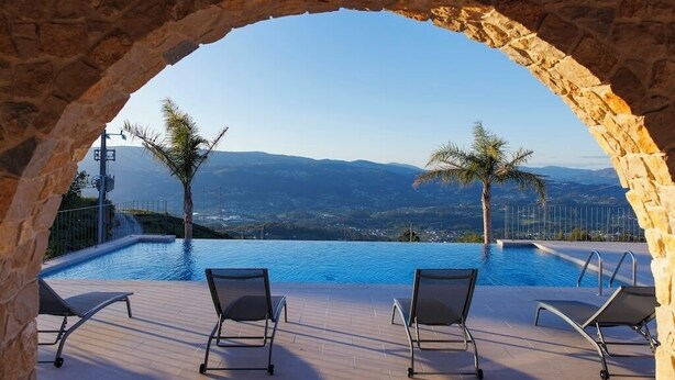 An infinity pool with a stone archway, two lounge chairs, and a view of distant mountains. - Vista D'Ouro- Luxury Villa in the mountains (Lavradas, Ponte da Barca)
