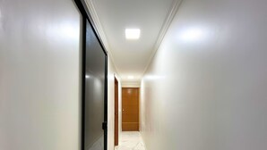Un pasillo con paredes blancas y suelo de mármol, que conduce a una puerta de madera al final.