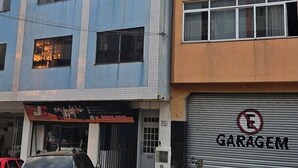 Un edificio de varios pisos con una puerta de garaje que dice 'GARAGEM' y un letrero con 'JC' sobre la entrada.