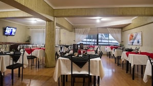 A restaurant with multiple tables, some with red tablecloths, and a television mounted on the wall. - Hotel Dikran (Los Angeles)