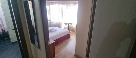 A hotel room with a bed, a small table, and a window with curtains.