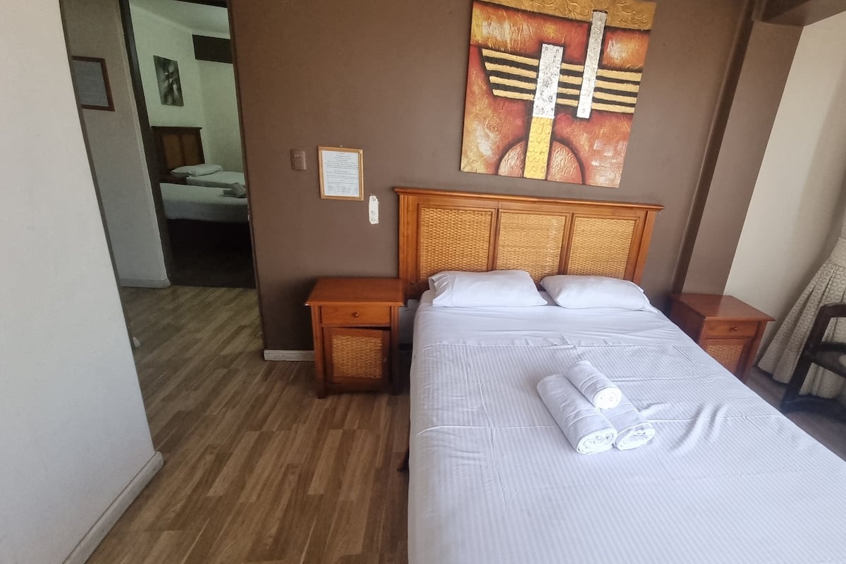 A hotel room with a large bed, wooden headboard, two bedside tables, a chair, and a painting on the wall.