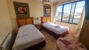 A hotel room with two beds, a window with a view of buildings, and artwork on the walls. - Hotel Dikran (Los Angeles)
