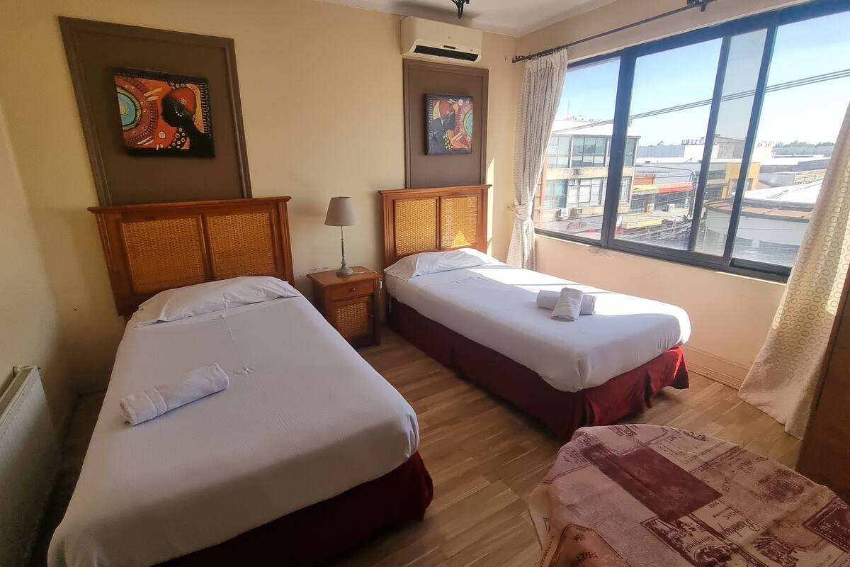 A hotel room with two beds, a window with a view of buildings, and artwork on the walls.