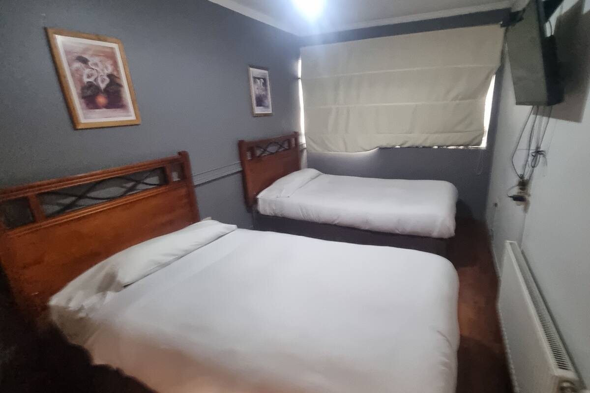 A room with two single beds, a wooden headboard, a framed picture on the wall, and a window with a white curtain.