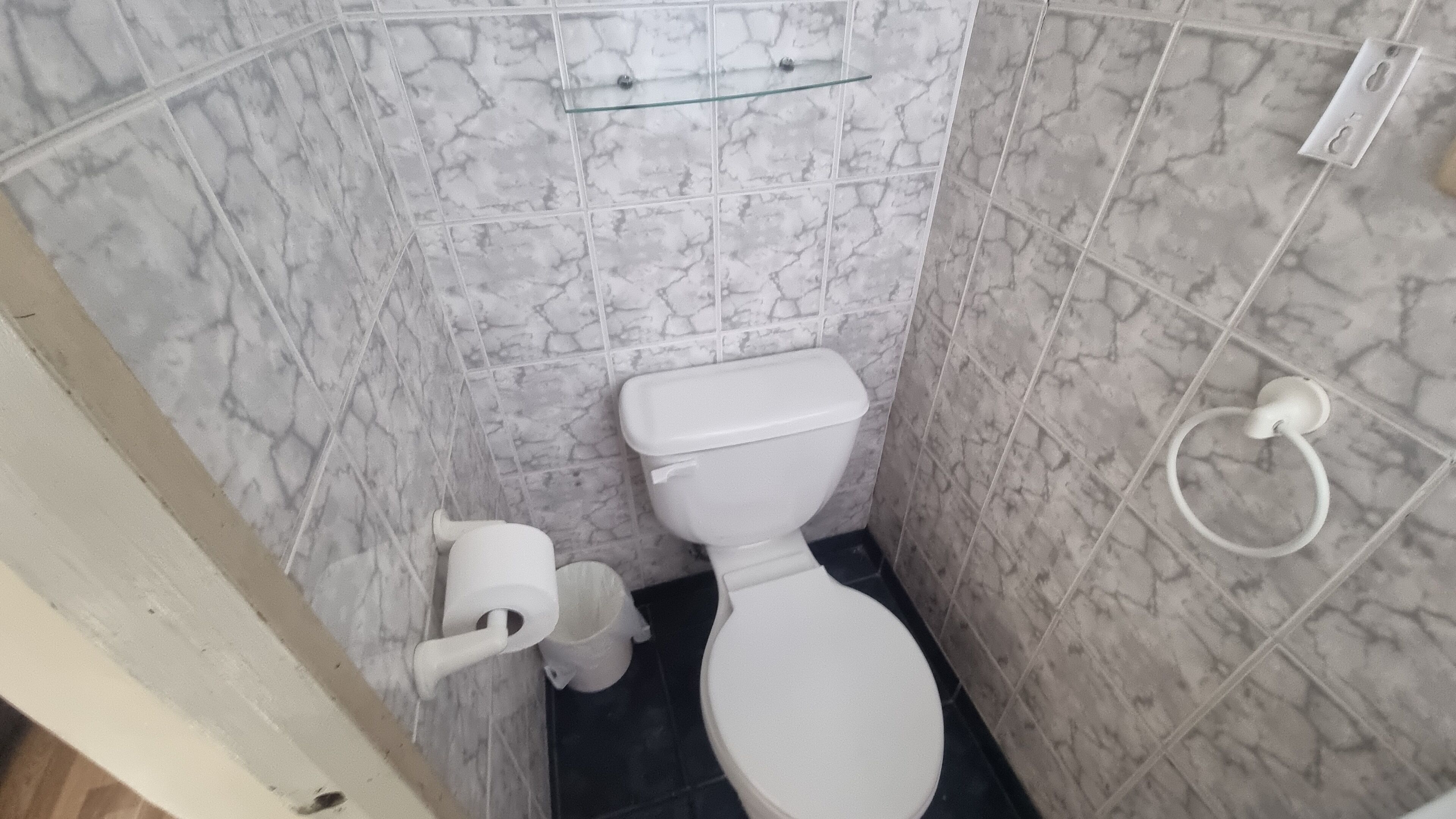 A small bathroom with a toilet, a glass shelf above the toilet, and a towel rack on the wall.