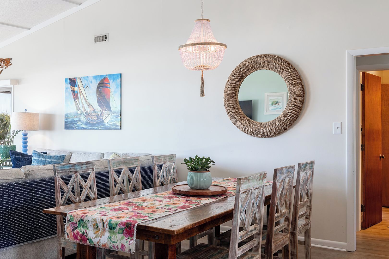 A dining area with a wooden table, floral tablecloth, and a woven mirror.