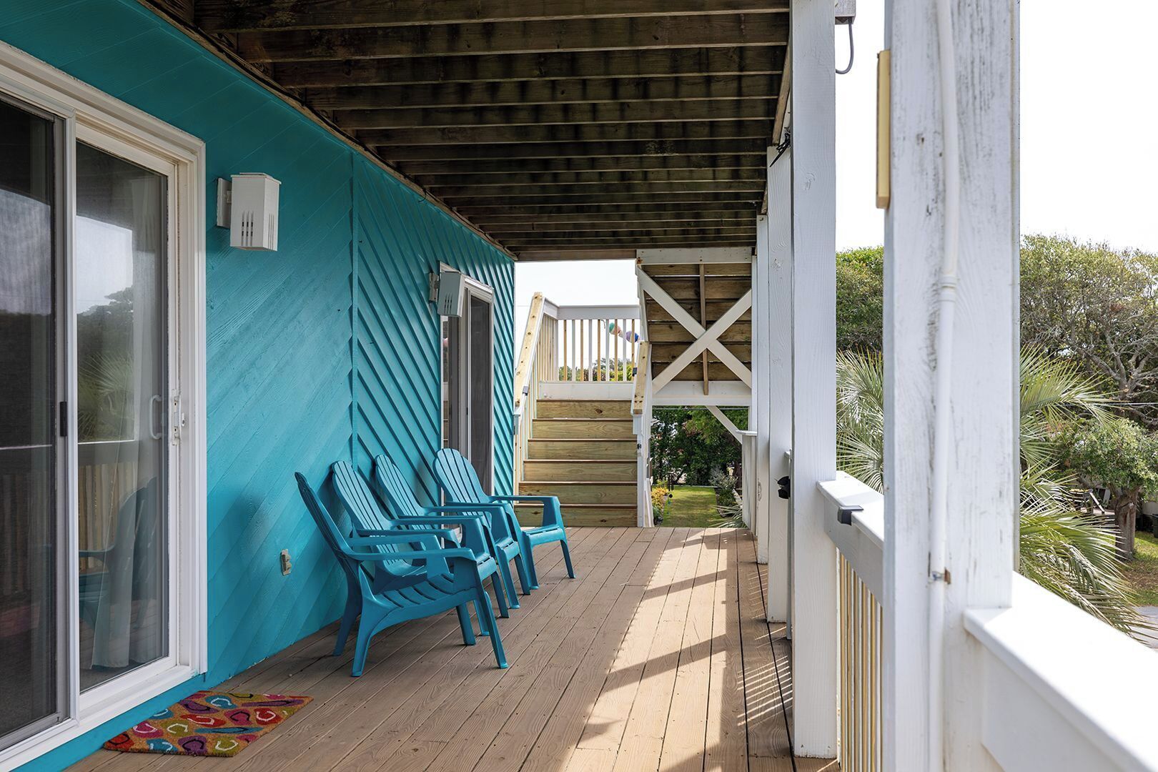 A covered porch with wooden flooring and blue Adirondack chairs.