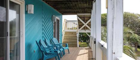 A covered porch with wooden flooring and blue Adirondack chairs.