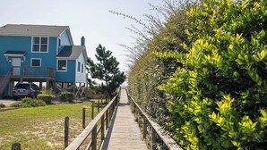 Une promenade en bois mène à une maison bleue dotée d’un porche et d’une voiture garée à proximité.