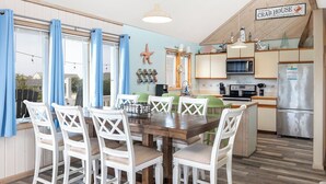 Une cuisine compacte avec un coin repas, comprenant une table en bois, des chaises blanches et un panneau au-dessus du réfrigérateur.