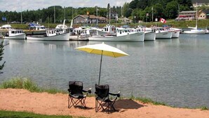 Dos sillas sobre arena junto a un lago, con barcos al fondo.