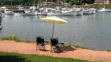 Enjoy lakeside relaxation with a row of boats moored in the water, perfect for boating or fishing. Two chairs and a shaded area invite you to unwind.
