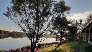 Vista de un lago con un pabellón, sillas y un camino que lleva a un edificio.