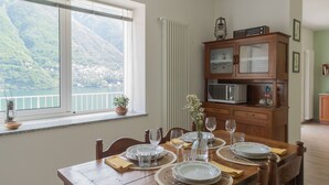 Un coin repas avec une table dressée pour quatre personnes, une vue sur un paysage montagneux par la fenêtre et un meuble en bois contenant des appareils de cuisine.