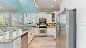 A modern kitchen with white cabinets, stainless steel appliances, and a granite countertop. - Coquina Sands - Pool Home with Beach Views - Powered by Island Real Estate (Holmes Beach)