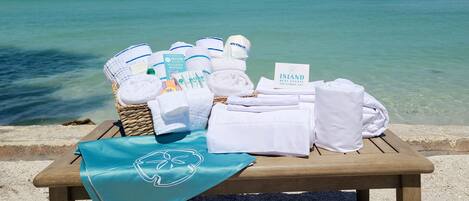 A wooden table with towels, toiletries, and a welcome mat by the beach.