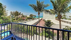 A balcony with a view of a beach, palm trees, and a parking lot. - Coquina Sands - Pool Home with Beach Views - Powered by Island Real Estate (Holmes Beach)