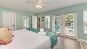 A bedroom with a bed, a ceiling fan, a view of a pool through the window, and a door leading to another room. - Coquina Sands - Pool Home with Beach Views - Powered by Island Real Estate (Holmes Beach)