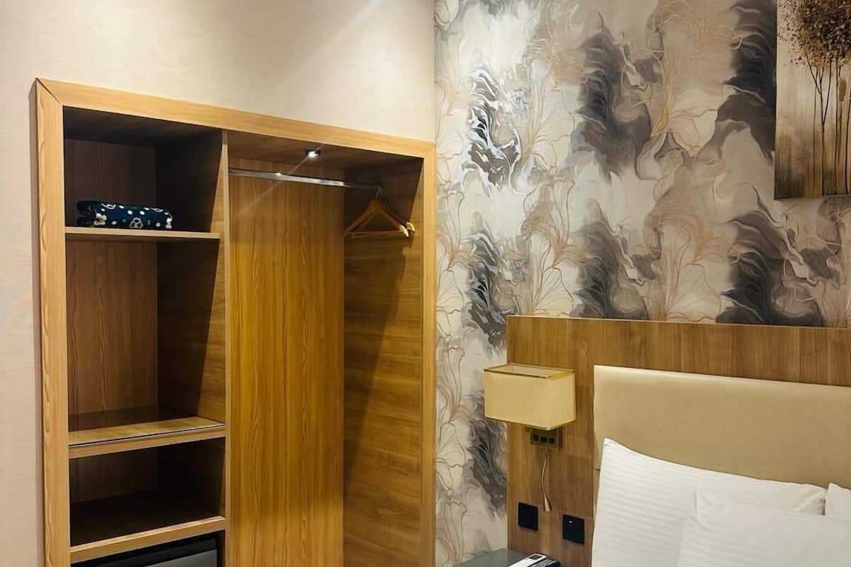 A hotel room with a bed, a wardrobe, a desk, and a wall with a floral pattern.