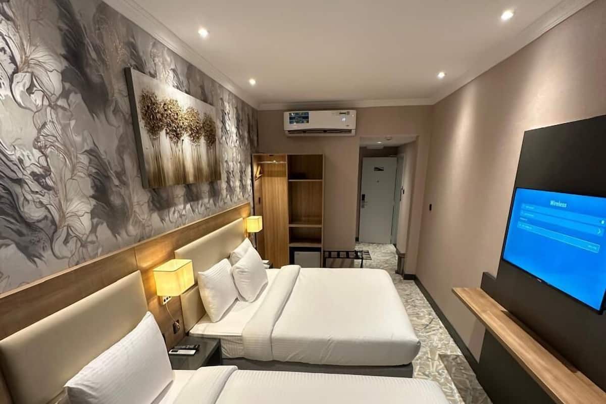 A hotel room with two beds, a TV, an air conditioning unit, and a wardrobe.