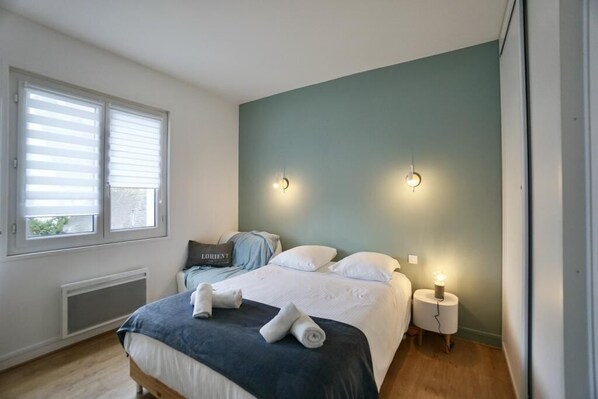 A bedroom with a bed, two bedside lamps, a window with blinds, and a radiator.