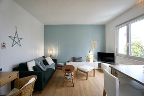 A modern living room with a sofa, a small table, a TV, and a window providing natural light.