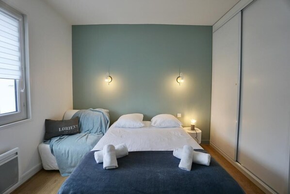 Une chambre à coucher avec un lit, des oreillers, une table de chevet et des lampes fixées au mur.