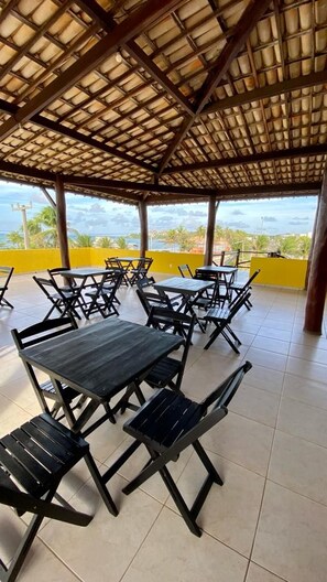 An outdoor patio with tables and chairs, a tiled floor, and a view of the ocean. - Pousada A Praia (Parnamirim)