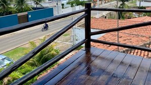 A wooden balcony with a view of a coastal road, palm trees, and a beach. - Pousada A Praia (Parnamirim)