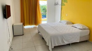 A bedroom with a bed, a TV, a small cabinet, and a window with curtains. - Pousada A Praia (Parnamirim)
