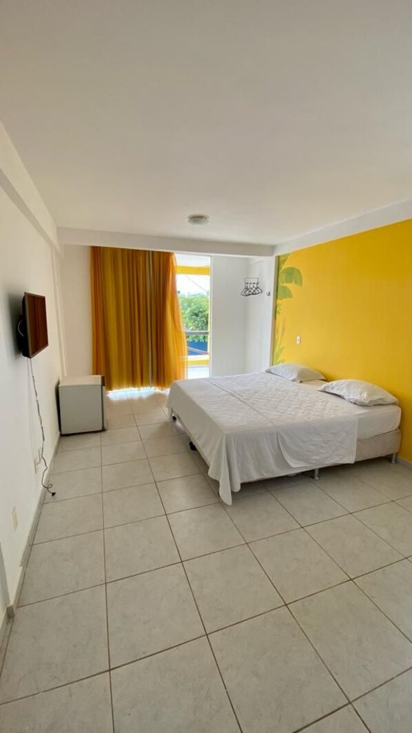 A bedroom with a bed, a television, and a window with curtains. - Pousada A Praia (Parnamirim)