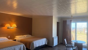 Quarto de hotel com duas camas, uma mesa com cadeiras, um radiador e vista pela janela.